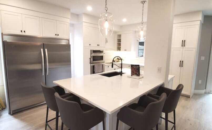 White shaker Kitchen. Side by side stainless steel fridge and freezer. Gray stools for island.